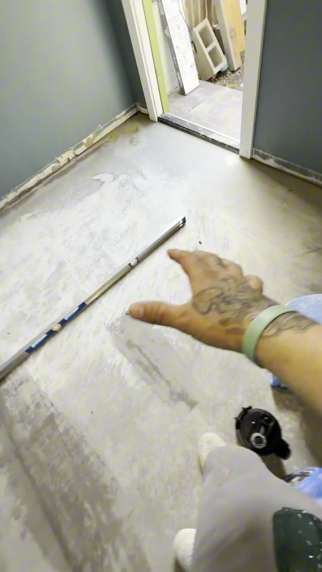 A long level laid across a freshly poured self-levelling floor, with a hand reaching toward it to check the surface