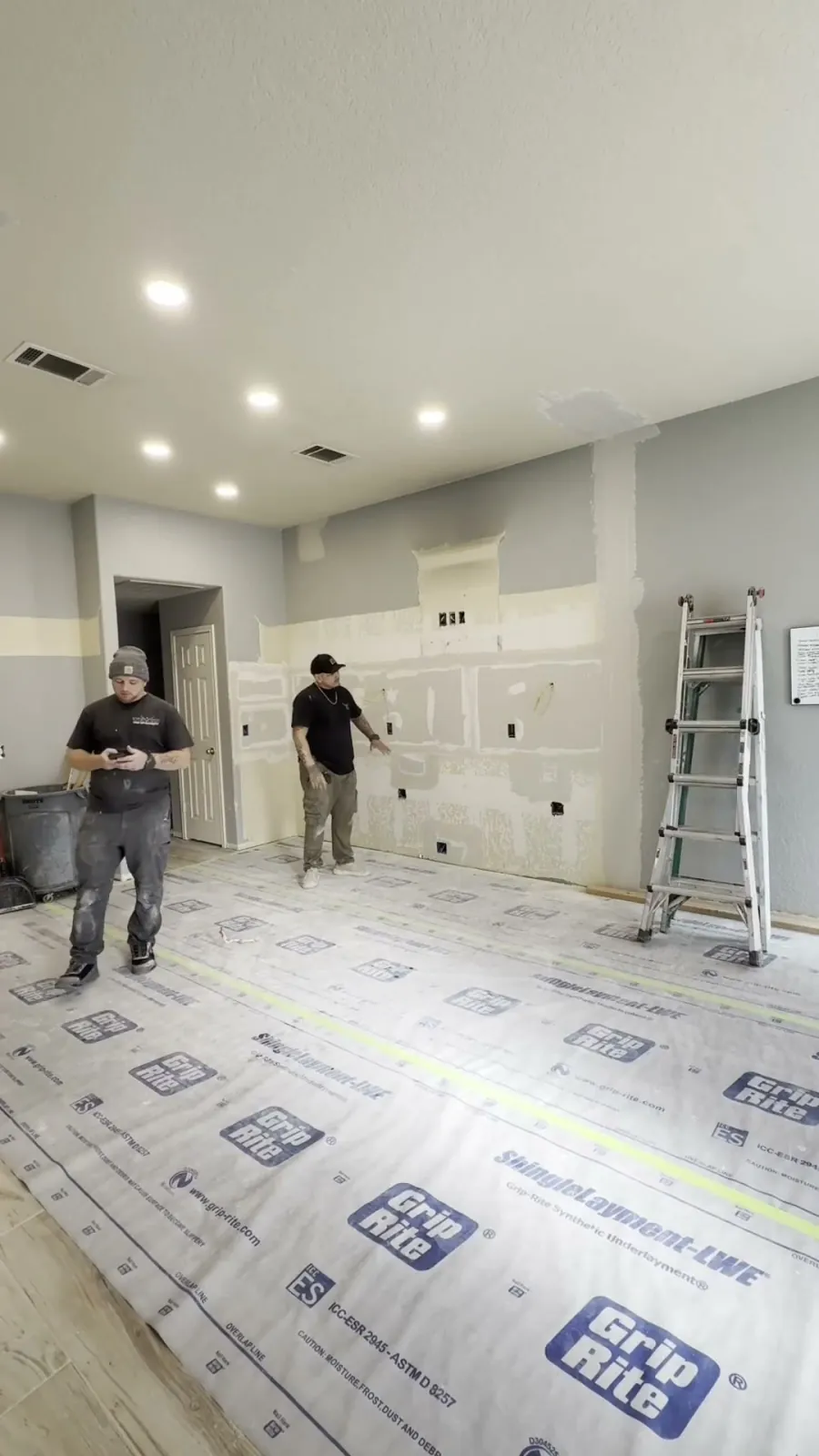 Kitchen walls drywalled and taped, floor covered in protective underlayment, before cabinets arrive