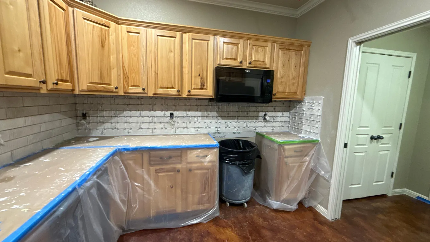 Kitchen mid-refresh with counters protected in plastic and the new tiled backsplash going up