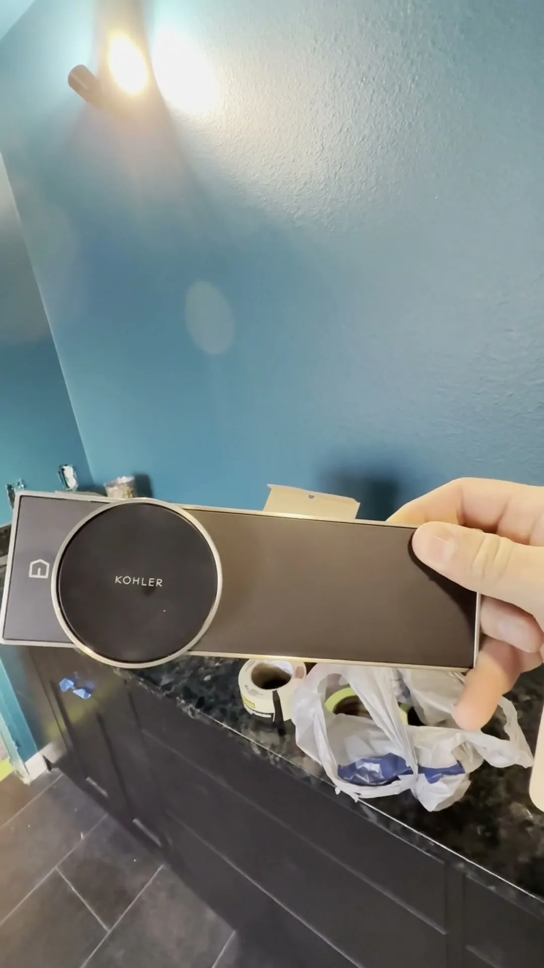 A crew member holding a shower control trim panel in front of a blue bathroom wall