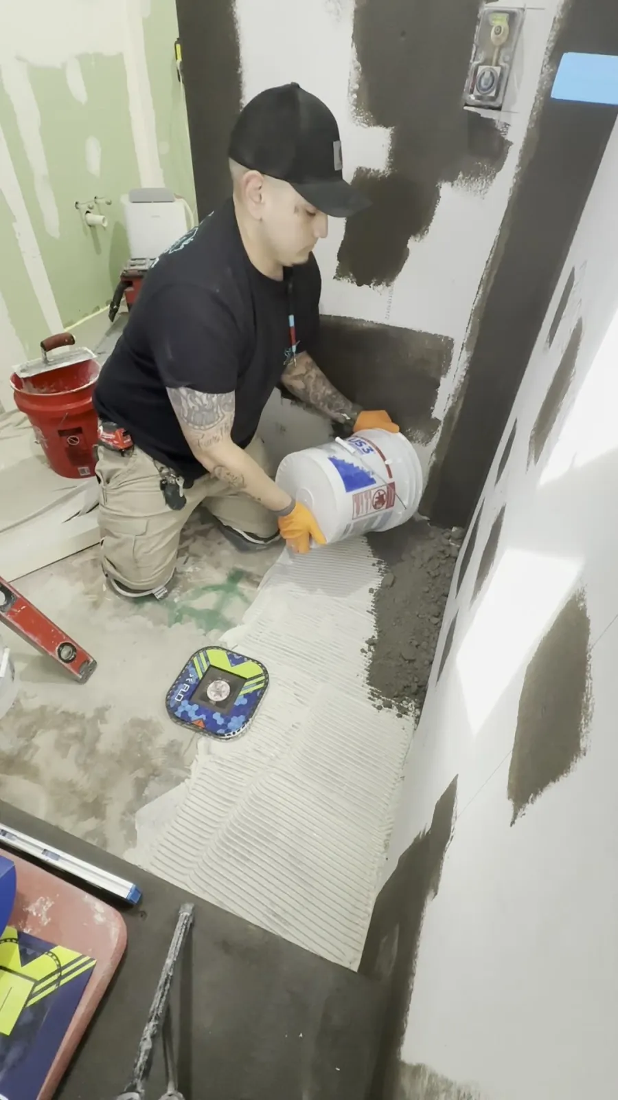 Waterproofing compound being worked across a shower wall with a level and trowel nearby