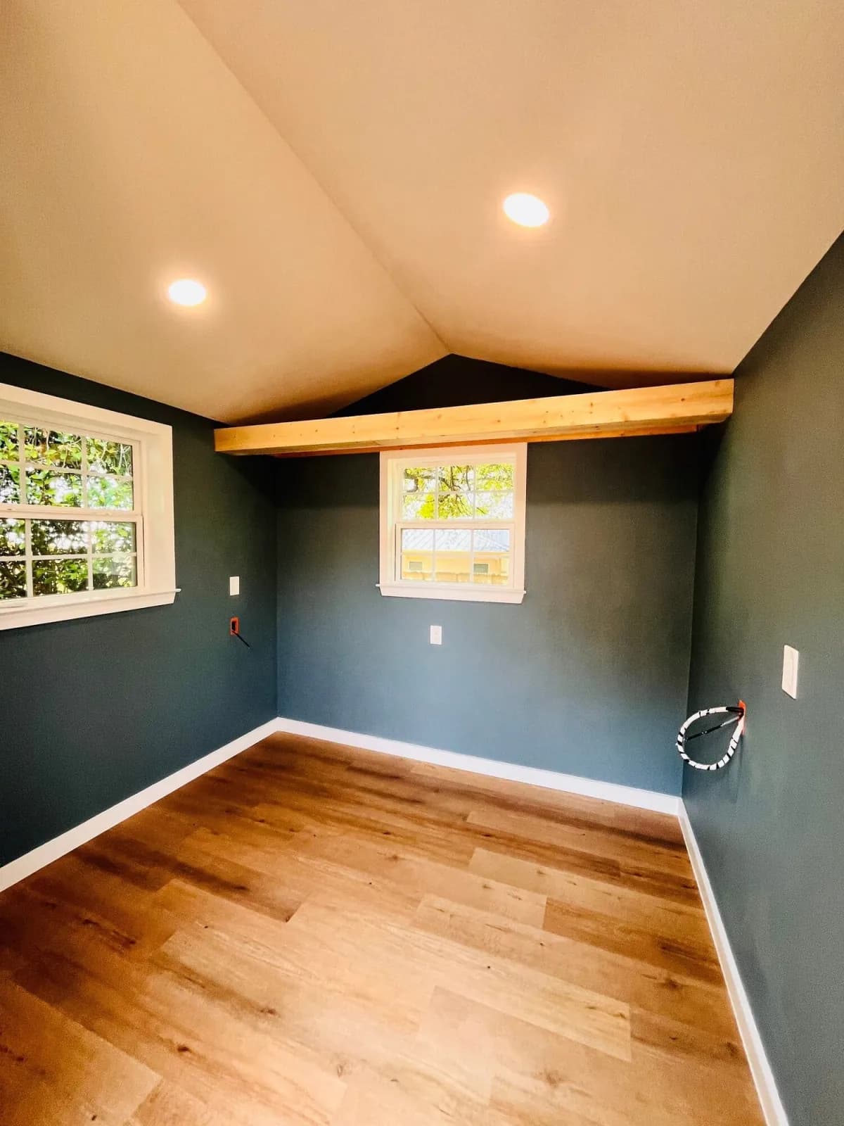 The finished studio interior: slate-blue walls, a vaulted ceiling with recessed lights, an exposed timber beam and wood-look plank flooring