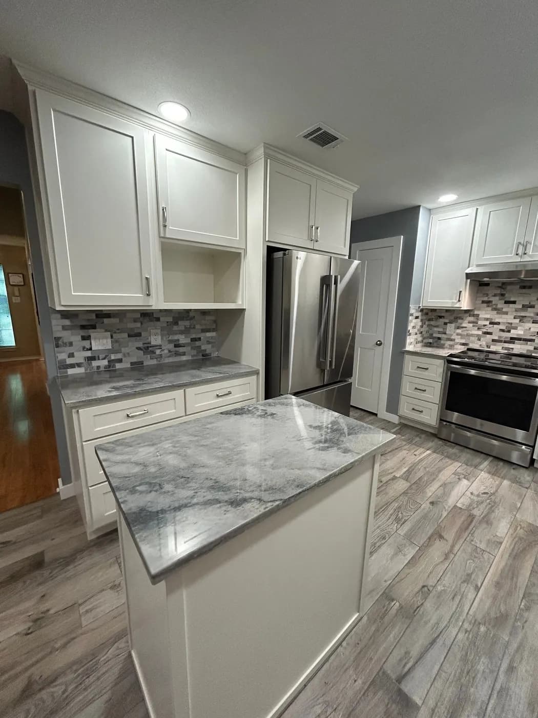 Finished kitchen with white shaker cabinets, a gray quartz island and stainless appliances