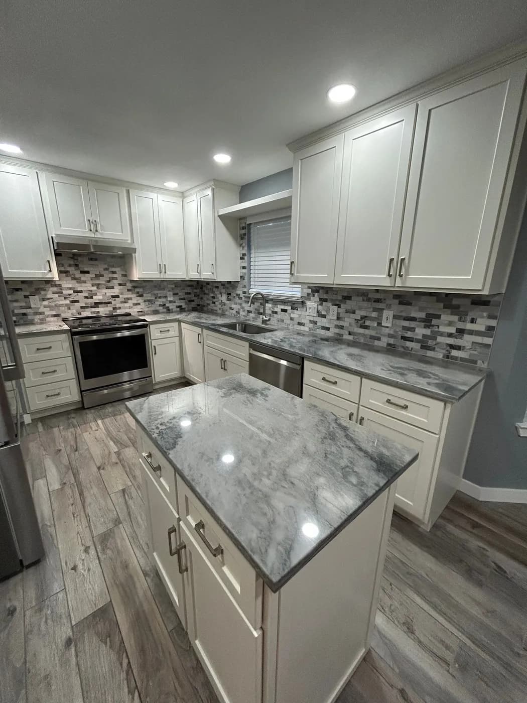 Quartz-topped island with white shaker cabinets and mosaic backsplash beyond