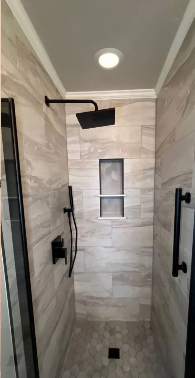 Finished tiled shower with black fixtures and a recessed niche