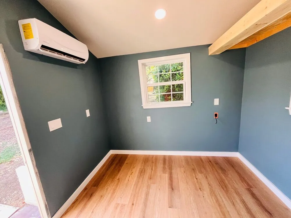 Corner of the studio with mini-split, window and exposed beam over plank flooring