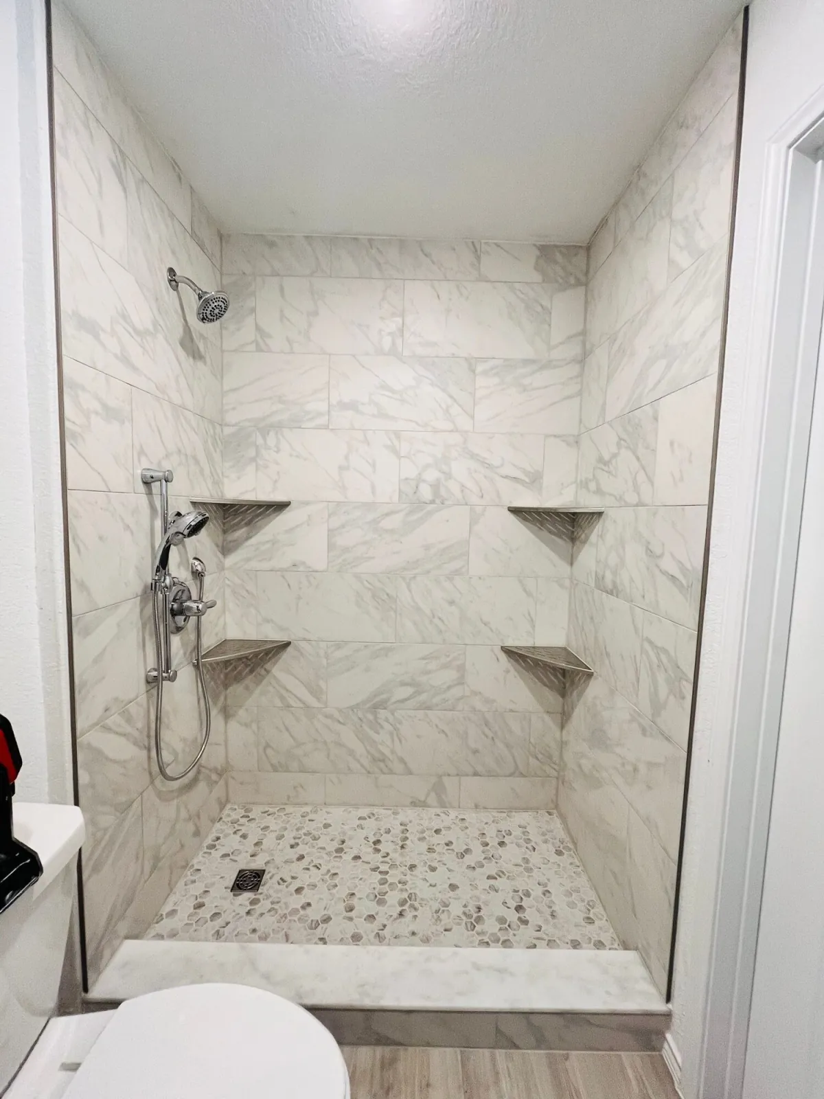 Walk-in shower with marble-look wall tile, twin corner shelves and a hex mosaic floor