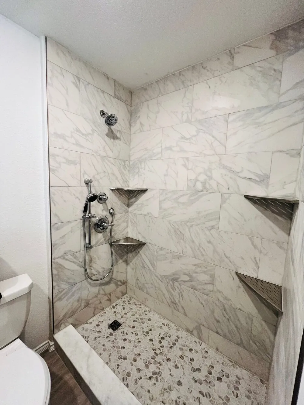 Shower alcove showing the metal corner shelves and handheld fixture against large-format tile