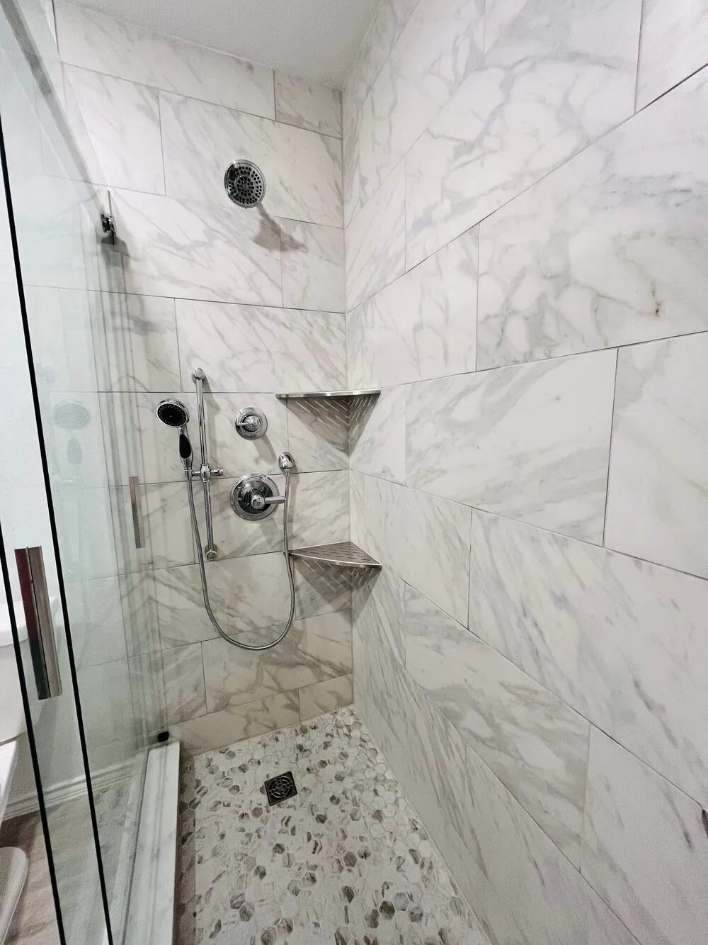 Glass shower door open to the hex mosaic floor and corner shelves