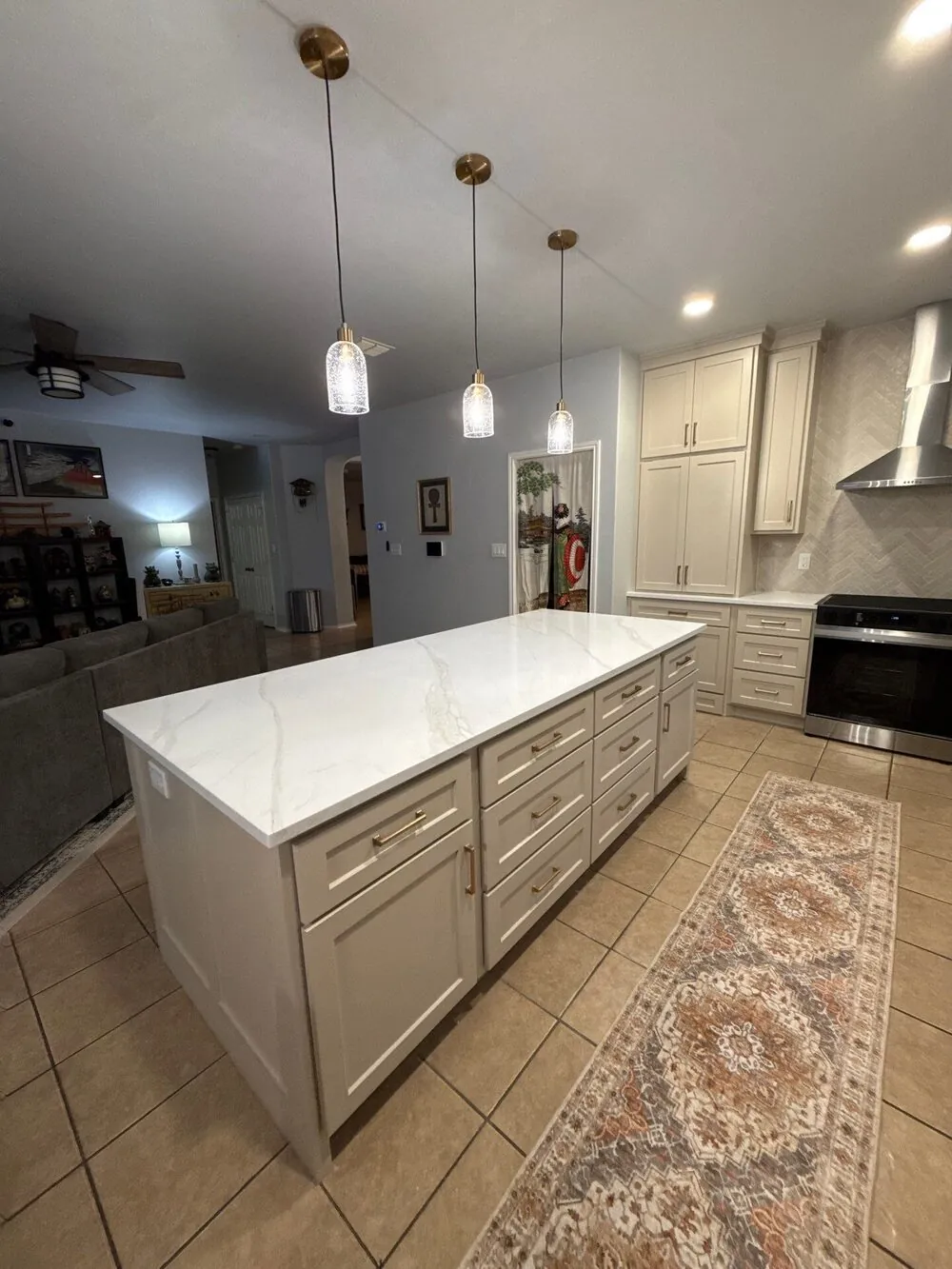 Kitchen island with quartz top under three pendant lights, looking through to the living area