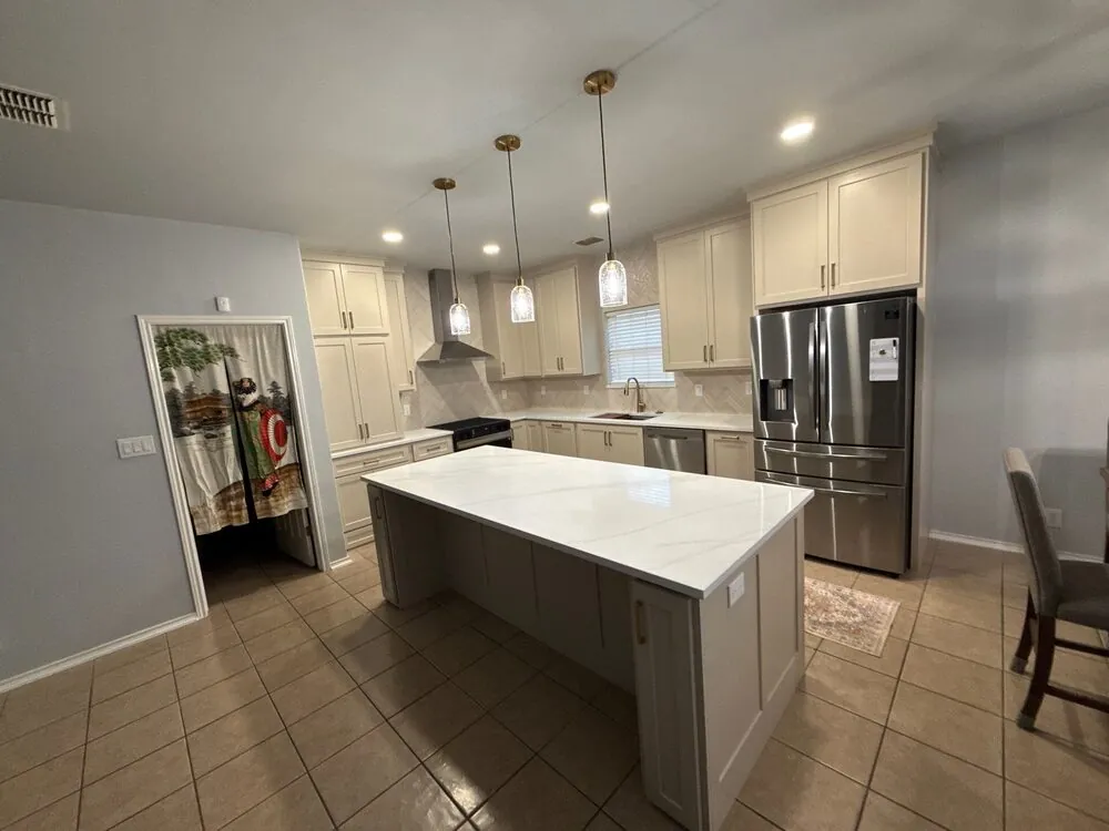 Kitchen from the doorway with the island, pendants and stainless refrigerator