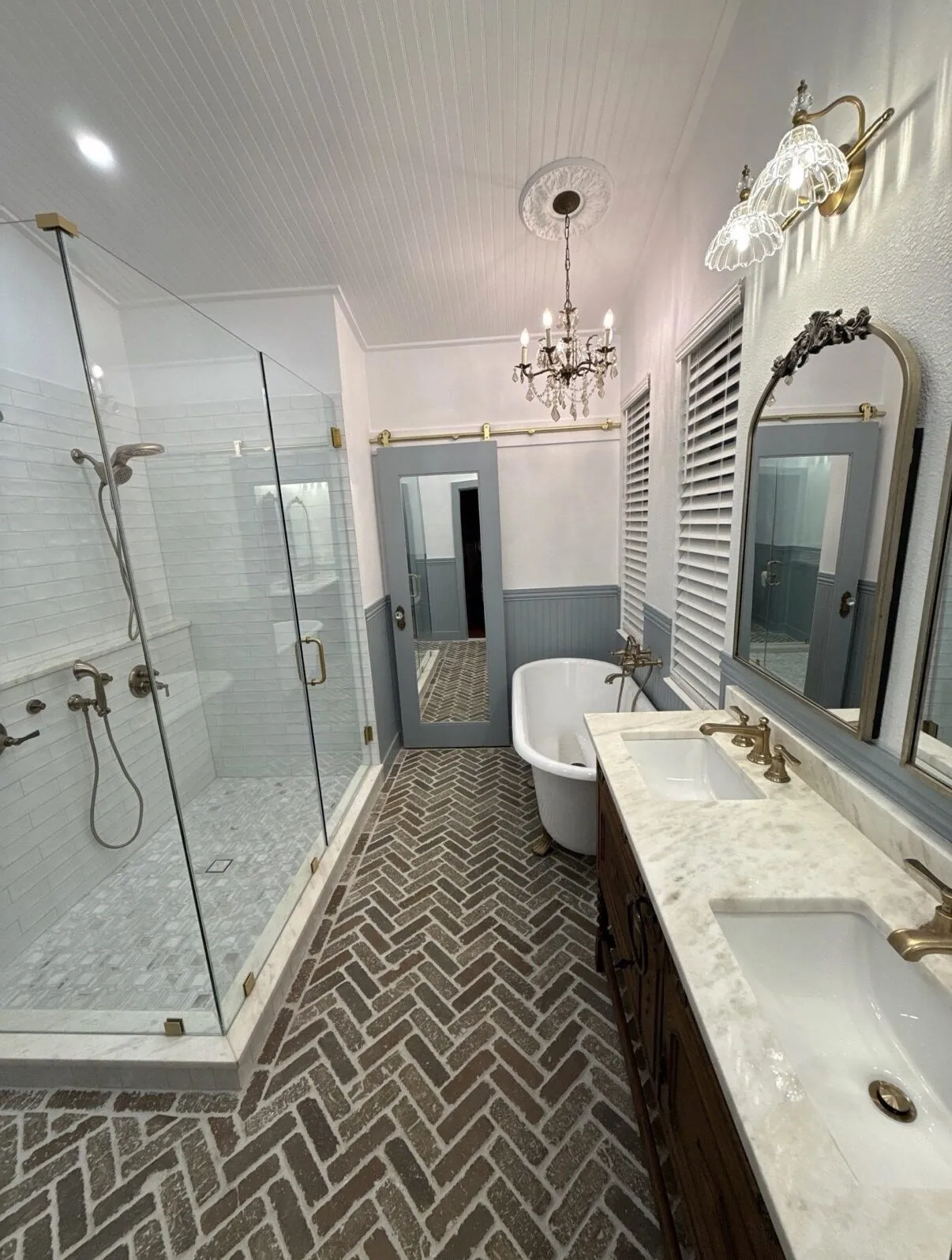 Shower enclosure and clawfoot tub seen across the herringbone floor