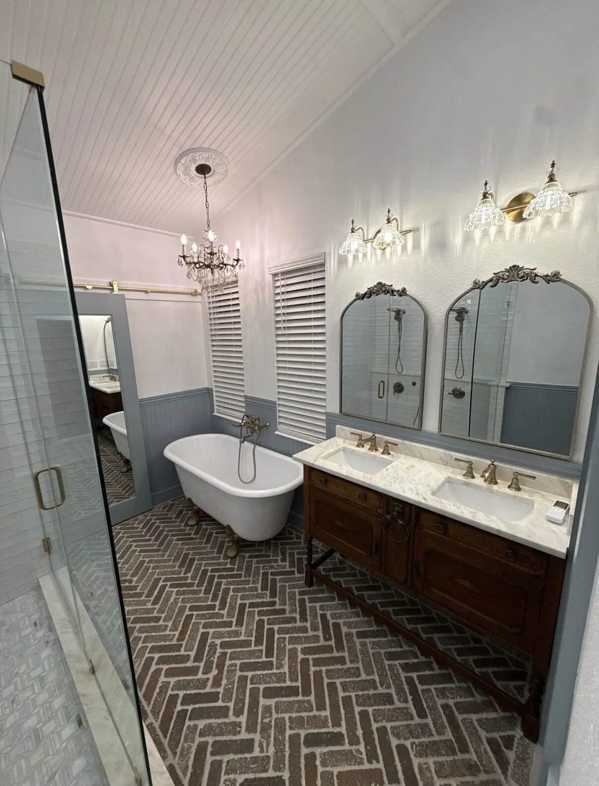 Clawfoot tub beneath a chandelier with the double vanity and arched mirrors beyond