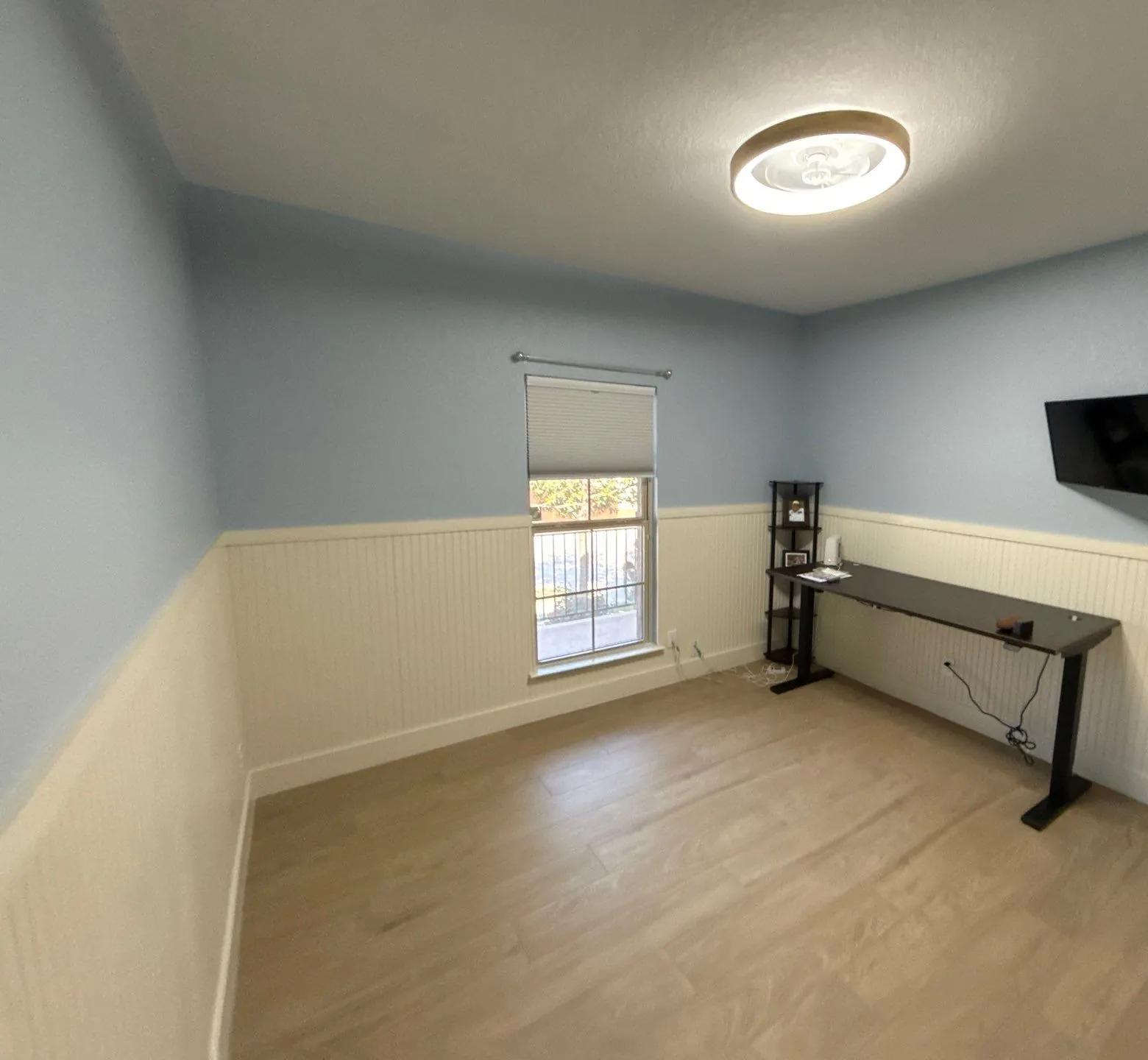 Wide view of the finished room showing the window, a wall-mounted television and a height-adjustable desk