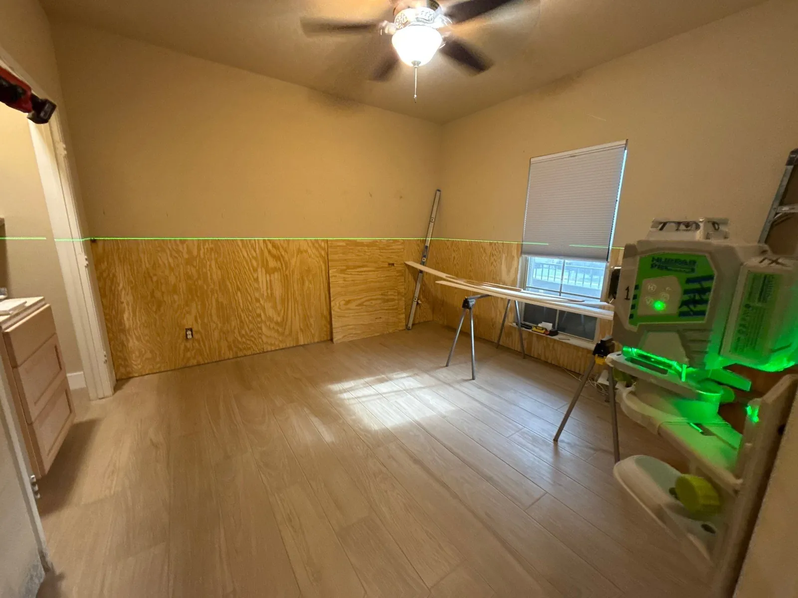A green laser line projected across the plywood substrate marking the height of the wainscot cap