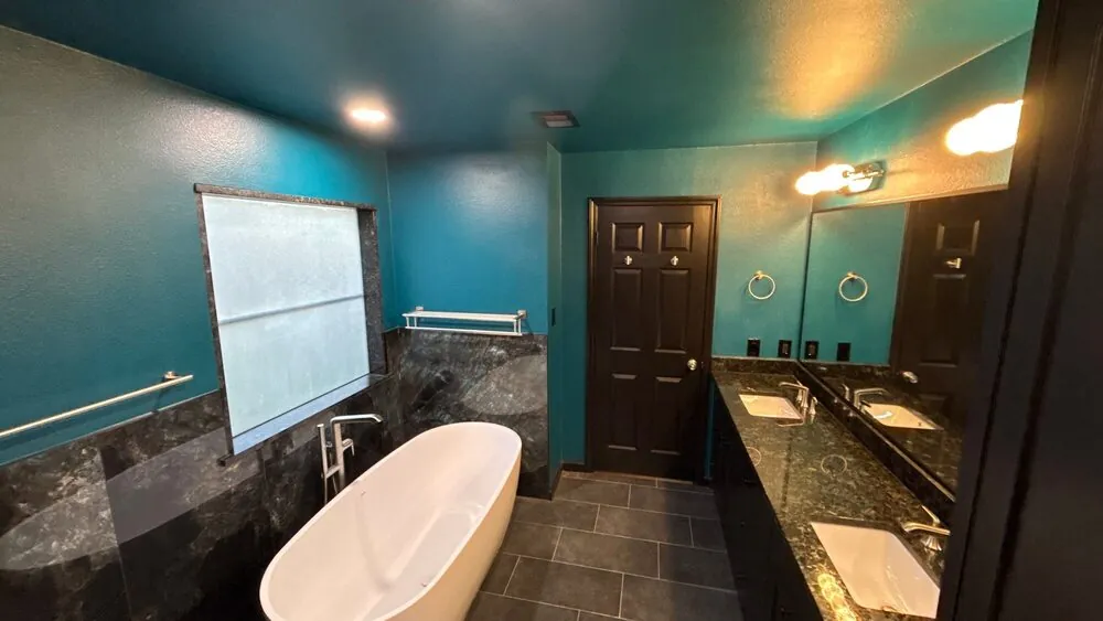 Teal bathroom walls with the tub, window and vanity in a single view