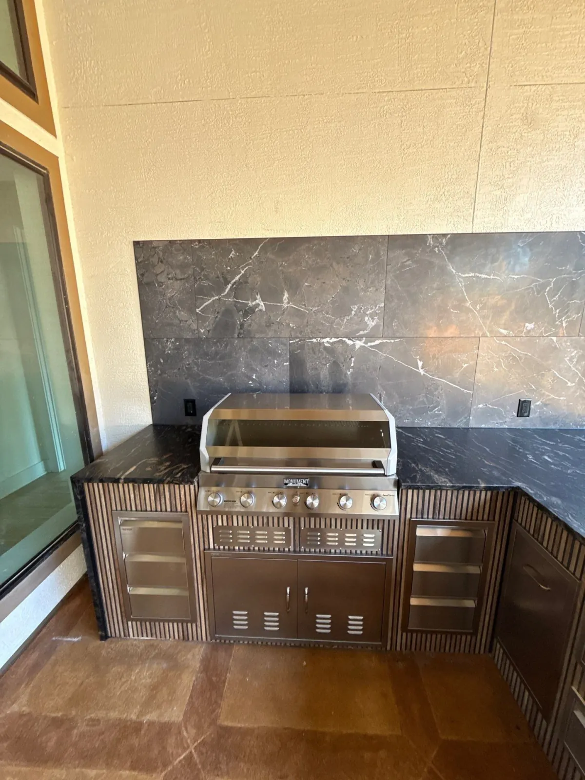 Finished outdoor kitchen with built-in grill, stainless doors and a marbled stone backsplash