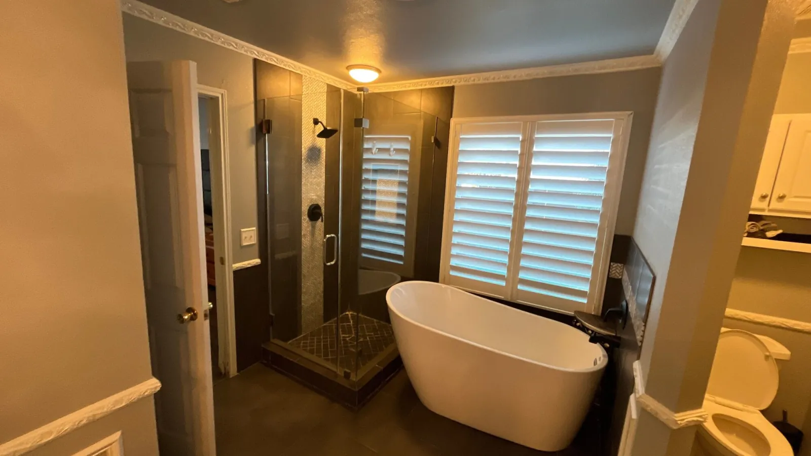 Freestanding tub and glass shower framed by plantation shutters