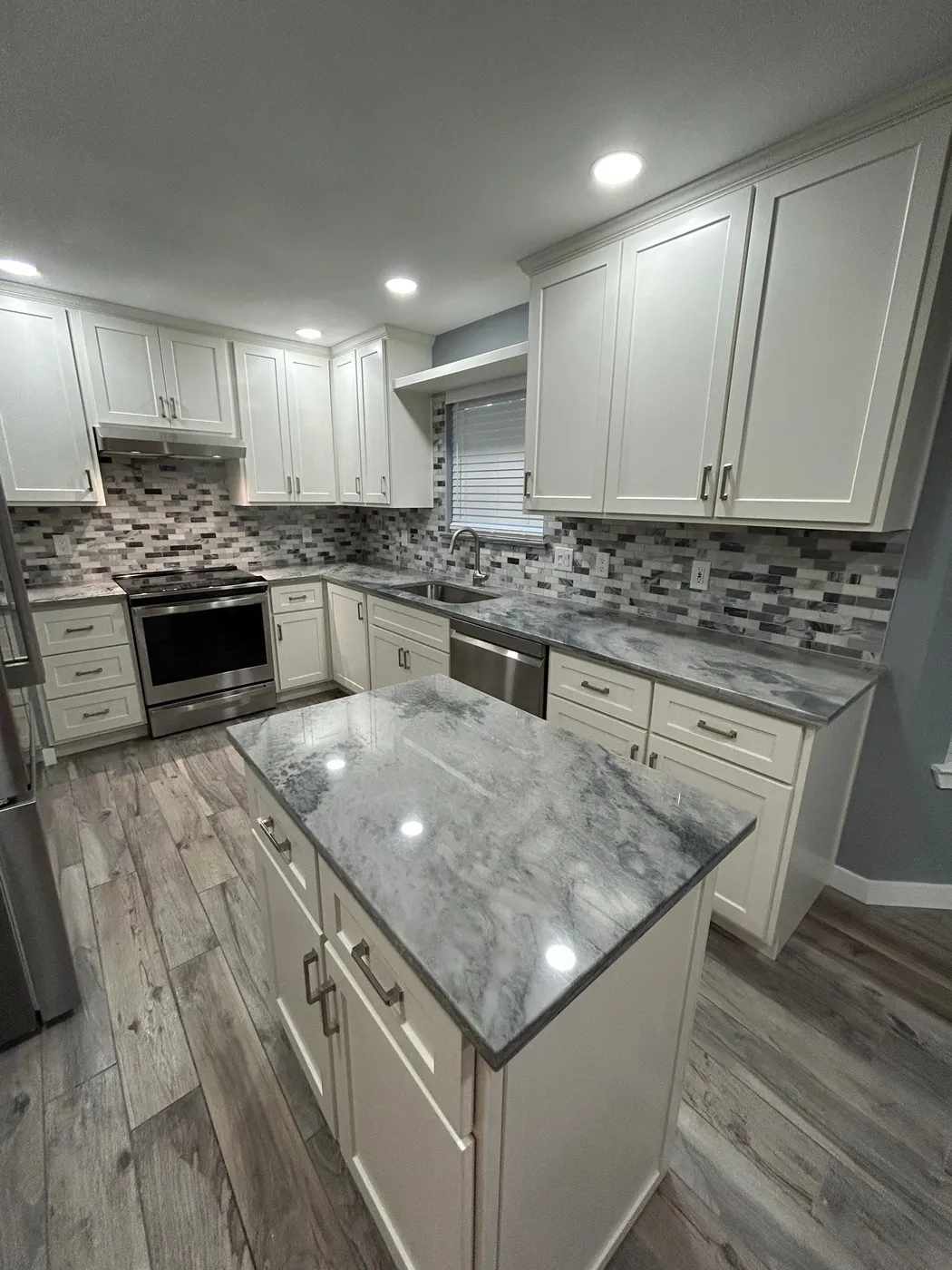 Quartz-topped island with white shaker cabinets and mosaic backsplash beyond