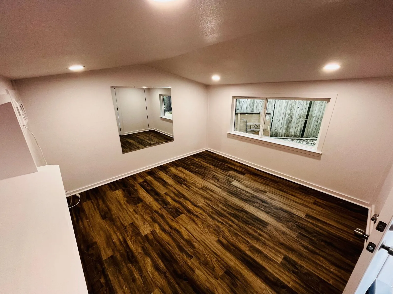 Finished studio with white walls, wood-look flooring and a wall-mounted mirror