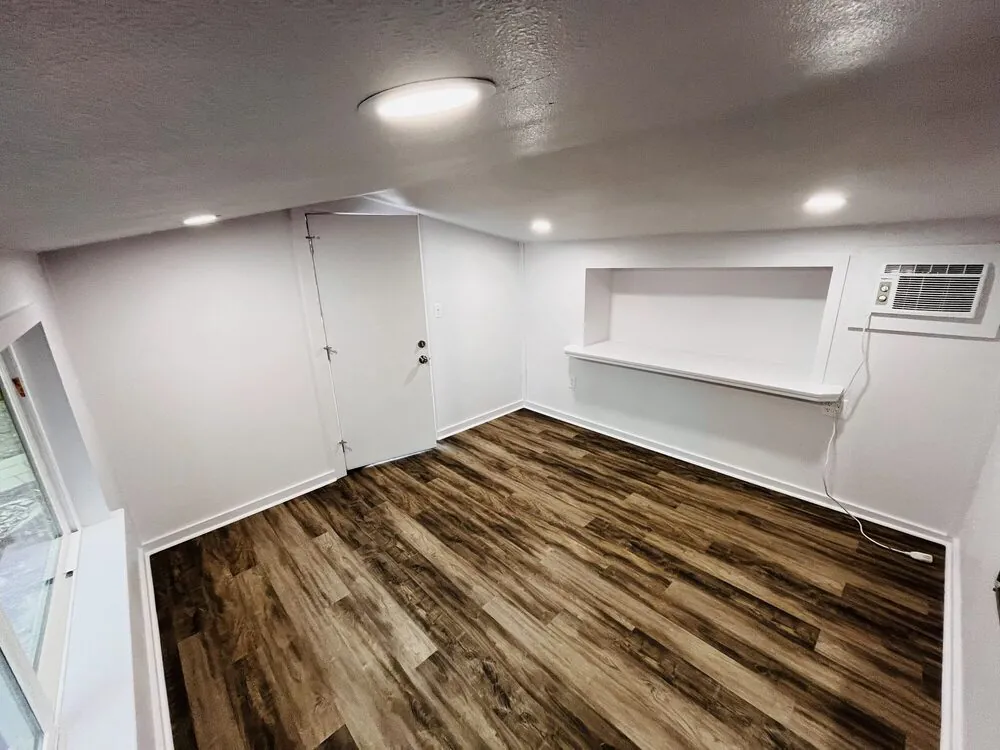 Studio interior with a built-in shelf, window air conditioner and wood-look flooring