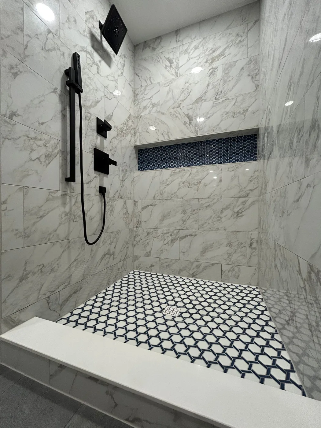 Walk-in shower with a black rain head and handheld on a slide bar, a navy mosaic niche band and patterned mosaic floor