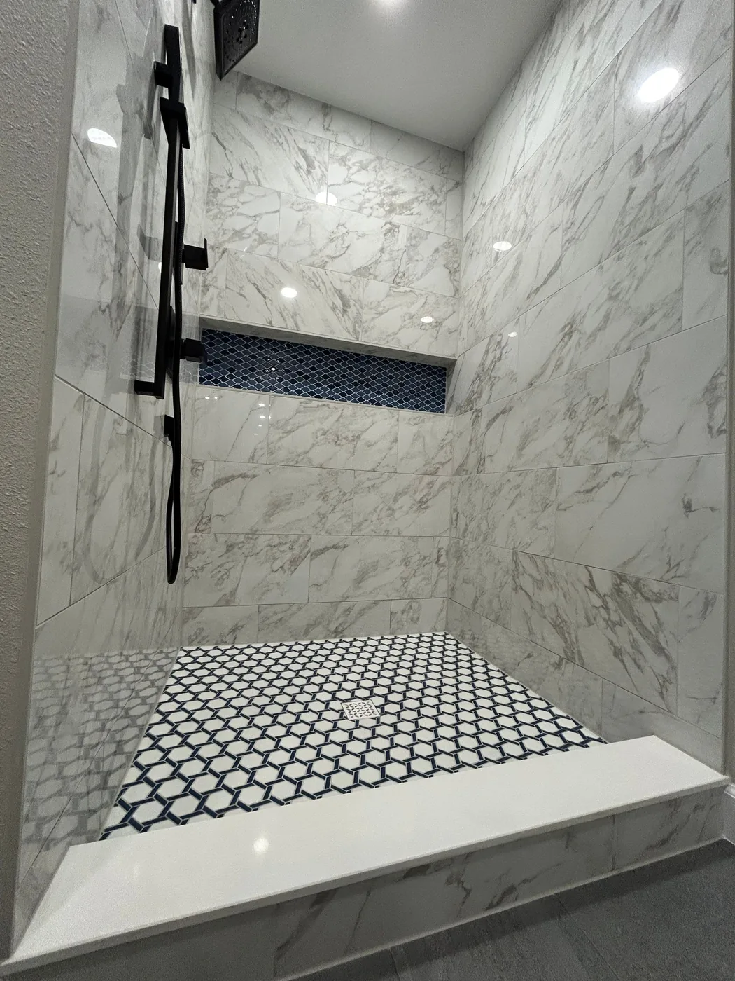 Shower wall in veined large-format tile with matte black controls and the niche running above the curb
