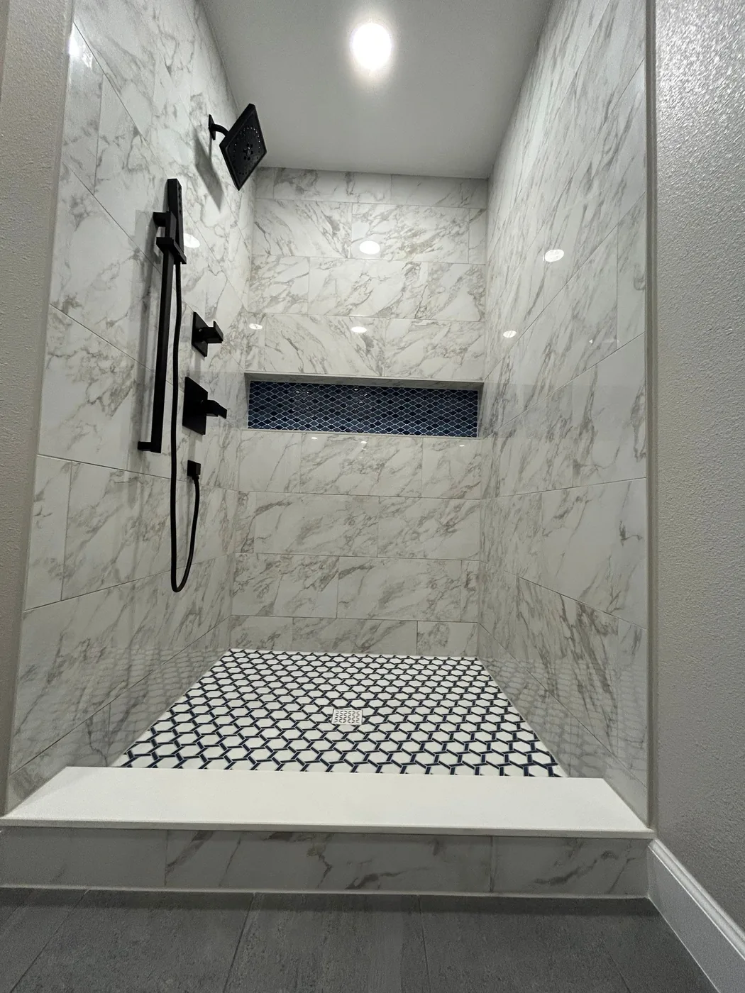 Shower corner showing the full height of the veined tile above the patterned mosaic floor