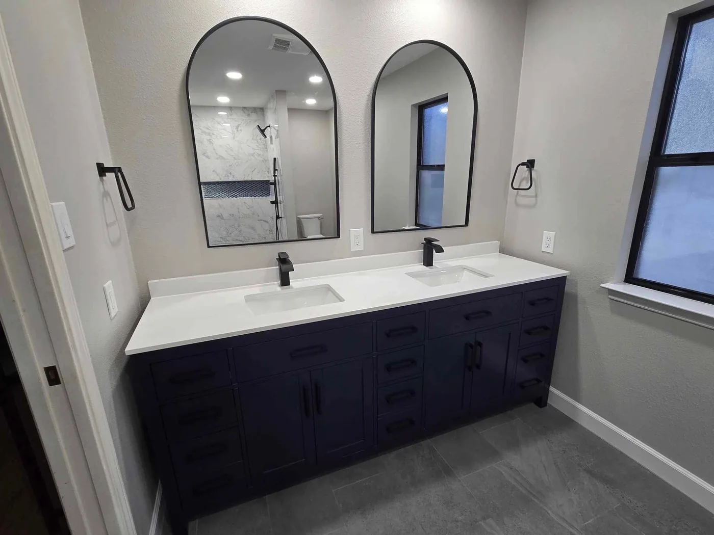 Double vanity with two arched mirrors, black faucets and a white countertop
