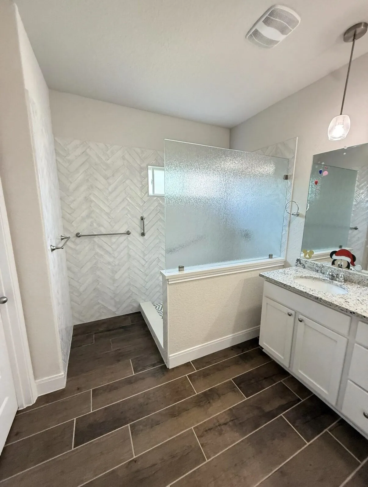 Bathroom with a herringbone-tiled walk-in shower, vanity and wood-look tile flooring